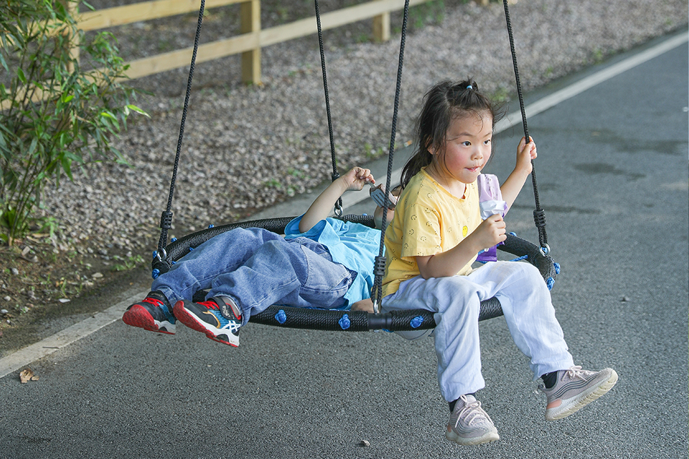 Ni&ntilde;a jugando en la plataforma nido columpio en el patio comercial - atracci&oacute;n de &aacute;rea de juego duradera